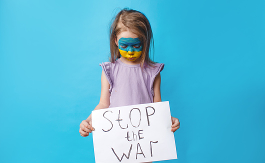 a sad girl with a split face in the colors of the Ukrainian flag holds an anti-war poster on a blue isolated background