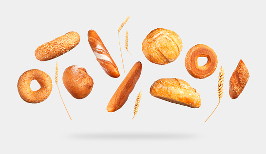 Various types of bread, ears of wheat flying on gray background. Classic wheat round bread, baguette, bun, sesame bagel. Organic Healthy Fresh isolated bread for bakery advertising. Food concept.