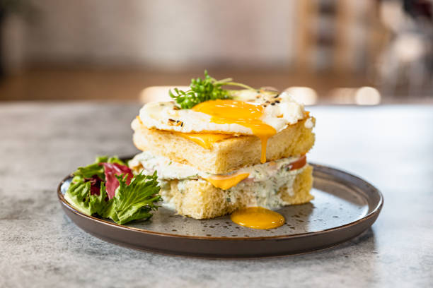 크로크 마담 ( croque madame) - 햄, 녹은 치즈, 계란 튀김, 샐러드소스를 곁들인 뜨거운 프렌치 샌드위치. 맛있는 아침 식사. - fried egg lettuce vegetable lunch 뉴스 사진 이미지