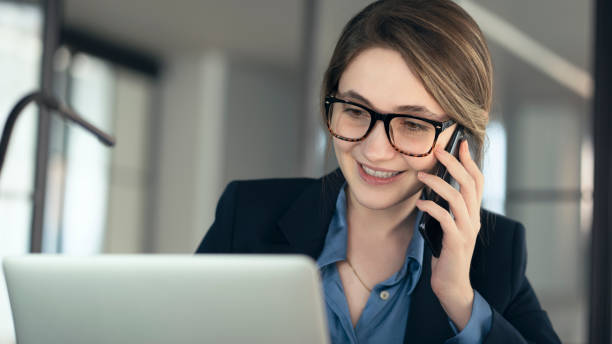 istock Young businesswoman talking mobile phone and using laptop computer in the office 1389183453