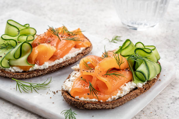 open sandwiches with salted salmon Rye bread open sandwiches with salted salmon and cucumber on a white stone table. Healthy food. stock fish stock pictures, royalty-free photos & images