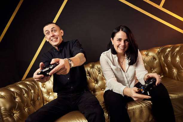portrait of crazy playful couple gamers having fun playing video games indoors sitting on sofa holding console gamepad in hands. rest at home, have a great weekend. x-box - xbox friends photos et images de collection