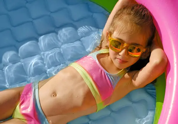 Photo of Kid in a swimsuit and sunglasses is cooling off in a small inflatable pool