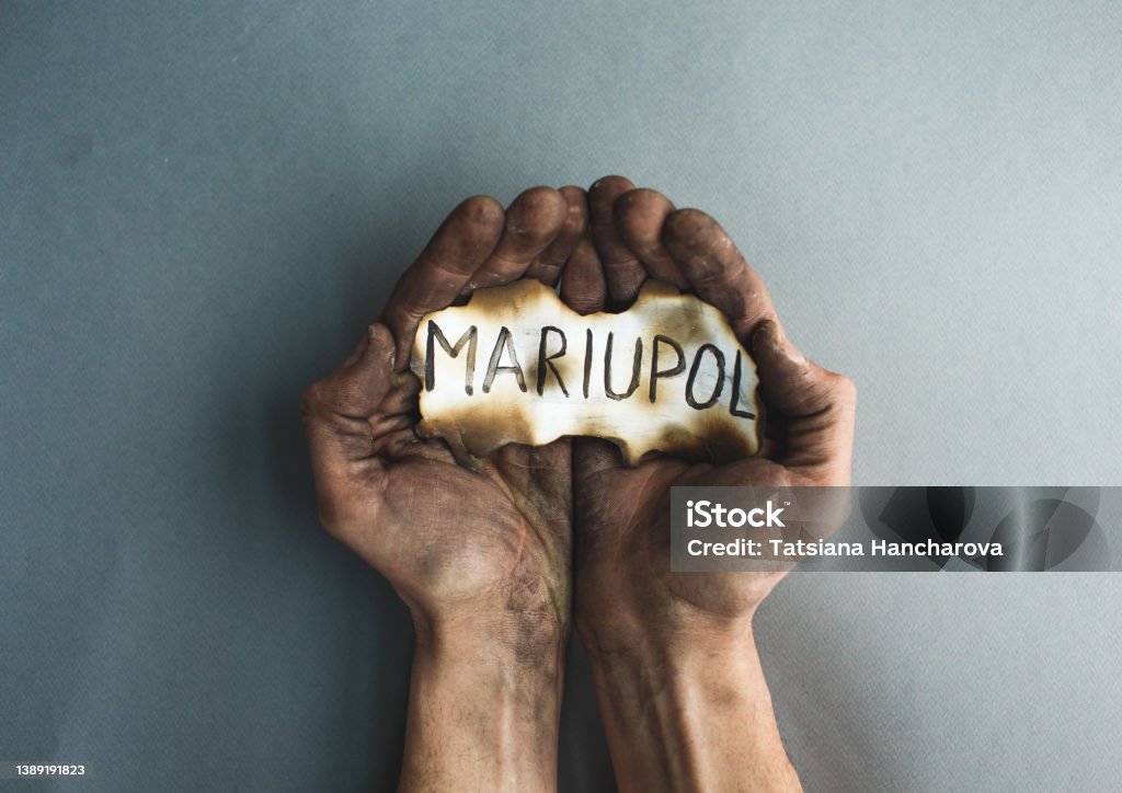 close-up of burnt male hands holding burnt paper with the inscription Mariupol. The war in Ukraine is a battle for the city close-up of burnt male hands holding burnt paper with the inscription Mariupol. The war in Ukraine is a battle for the city. Mariupol Stock Photo