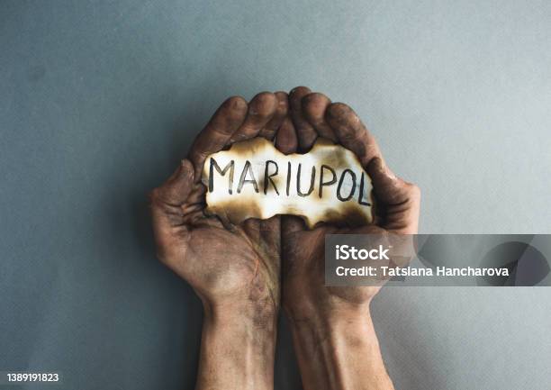 Closeup Of Burnt Male Hands Holding Burnt Paper With The Inscription Mariupol The War In Ukraine Is A Battle For The City Stock Photo - Download Image Now