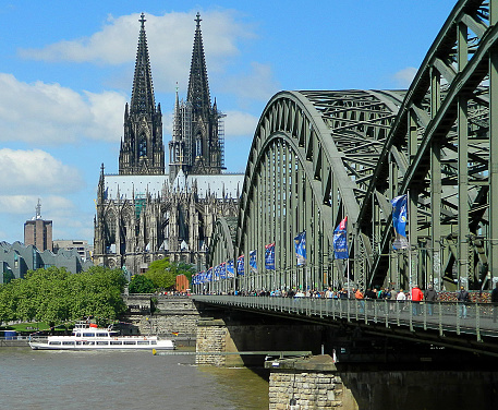 Cologne, Germany - May 31, 2013: Panoramic view of Cologne from Hohenzollern Bridge with Cologne Cathedral. People walks on bridge on a sunny day.There is a ship on Rhine River in cologne, Germany. Construction of Cologne Cathedral commenced in 1248 and was halted in 1473, leaving it unfinished. Work restarted in the 19th century and was completed, to the original plan, in 1880. It's a Roman Catholic cathedral in Cologne, Germany.
