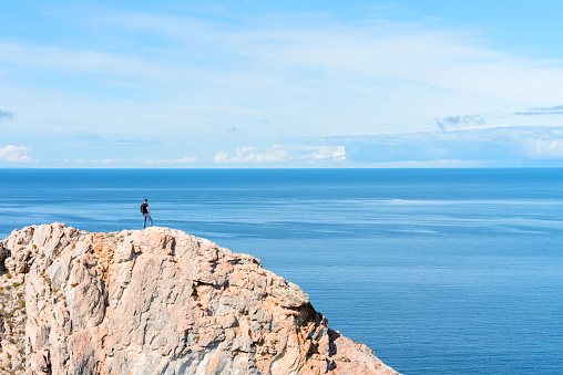 Man with backpack standing on a rock at the end of earth watching on the bright blue lake. Hiking or travel concept. Exploring the great outdoors. Beauty of nature.