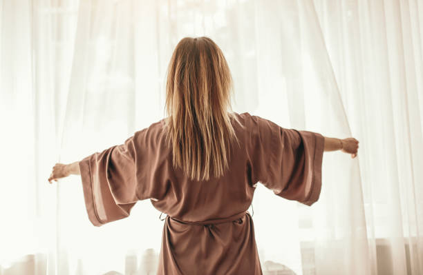 istock Woman waking up and opening curtains 1389206491