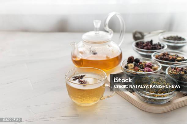 Glass Cup With Hot Tea And A Kettle On A Bright Table By The Window Tray With Different Varieties Of Herbal Tea On A White Background Delicious And Healthy Drink To Strengthen Immunity Space For Text Stock Photo - Download Image Now