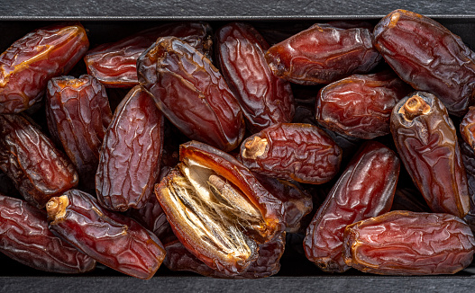 Pile of dates and seeds of date palm fruit close-up.Close-up view of ripe Medina dates pile in a small black metal bowl bowl on black wooden background.