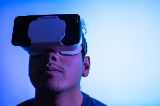 istock Young latin man using Virtual Reality VR Headset 3D Glasses. Blue Screen backdrop. Low key 1389219698