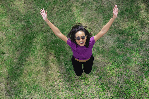 High angle view shot of smiling Asian woman jumping in the garden.