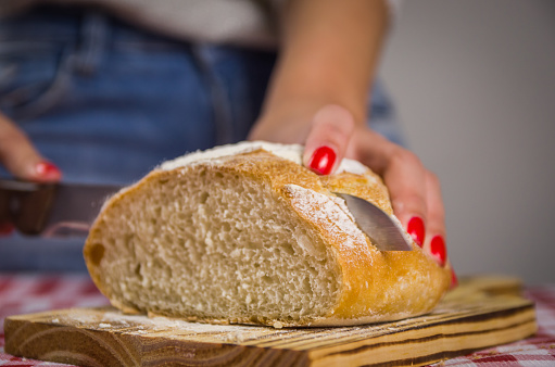 Beautiful Sourdough bread being sliced by knife by woman's hands and blurred background
