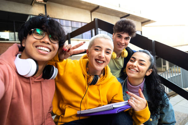 groupe multiracial d’amis d’université prenant un selfie avec téléphone à l’extérieur du bâtiment universitaire. les élèves rient. s’amuser - teenager adolescence campus group of people photos et images de collection