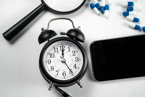 Alarm clock, computer, magnifying glass, calculator and medicine on white background board