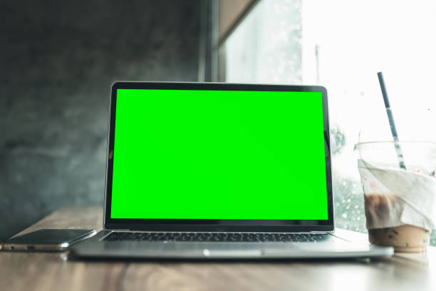 istock Mockup of laptop computer with empty screen with coffee and smartphone isolate on wooden office desk in coffee shop like the background ,Green screen 1389242189