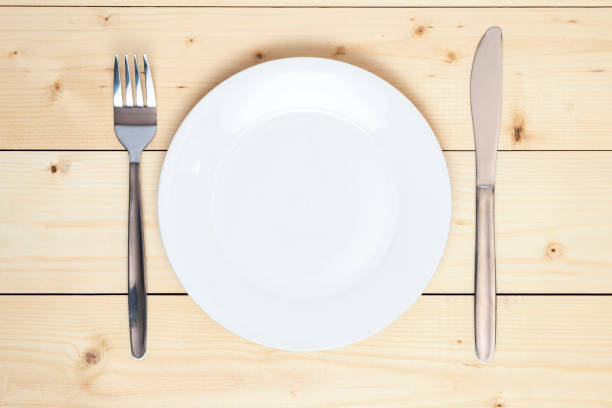 istock Top view of an empty white plate, fork and table knife on a wooden background 1389242795