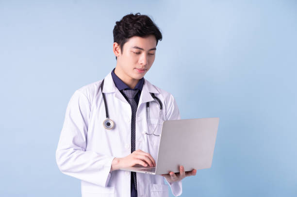 портрет молодого азиатского врача на синем фоне - dentist asian ethnicity portrait male стоковые фото и изображения
