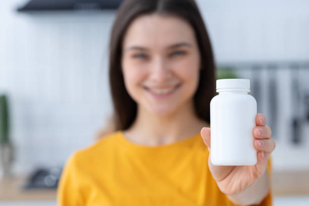 happy young caucasian woman holding bottle of dietary supplements or vitamins in her hands. close up. healthy lifestyle concept - bottle vitamin pill nutritional supplement white imagens e fotografias de stock