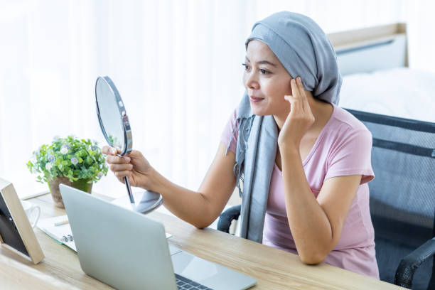 asian women disease mammary cancer patient lady looking at mirror with pink ribbon wearing headscarf After treatment to chemotherapy with working business at laptop in office at home,medicine concept mujer asiática enfermedad cáncer de mama paciente dama mirando al espejo con cinta rosa usando pañuelo en la cabeza después del tratamiento a la quimioterapia con negocios de trabajo en la computadora portátil en la oficina en casa, concepto de medici