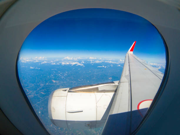 飛行中の飛行機の翼は、乗客の窓から見えます。青い空には白い雲が広がっています。 - mountain range earth sky airplane ストックフォトと画像