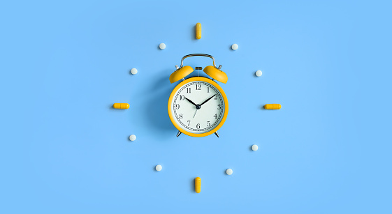Alarm Clock with tablets,pills, capsules on blue background, top view. Medication schedule and health concept