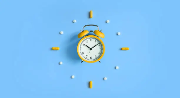 Photo of Alarm Clock with pills, medical capsules on blue background