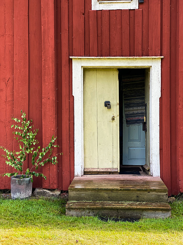 Old red wood panel house with bright green door. Scandinavian arcitecture. Allmoge. Scandinavian folklore. Rustic historical home. Welcoming open door. Summer vacation in sweden. Historical building.