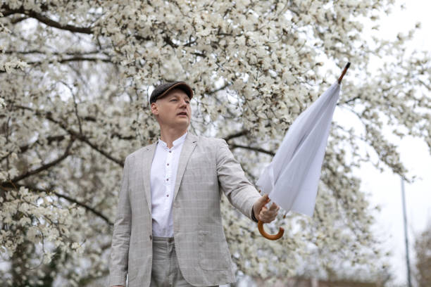 schöner lächelnder mann mit regenschirm inmitten einer weiß blühenden magnolie - 45 hochzeitstag stock-fotos und bilder