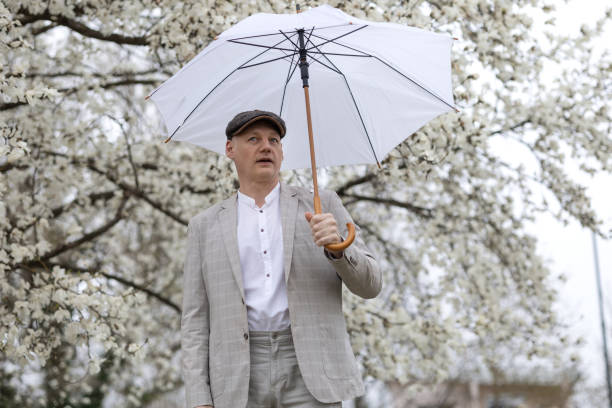 schöner lächelnder mann mit regenschirm inmitten einer weiß blühenden magnolie - 45 hochzeitstag stock-fotos und bilder