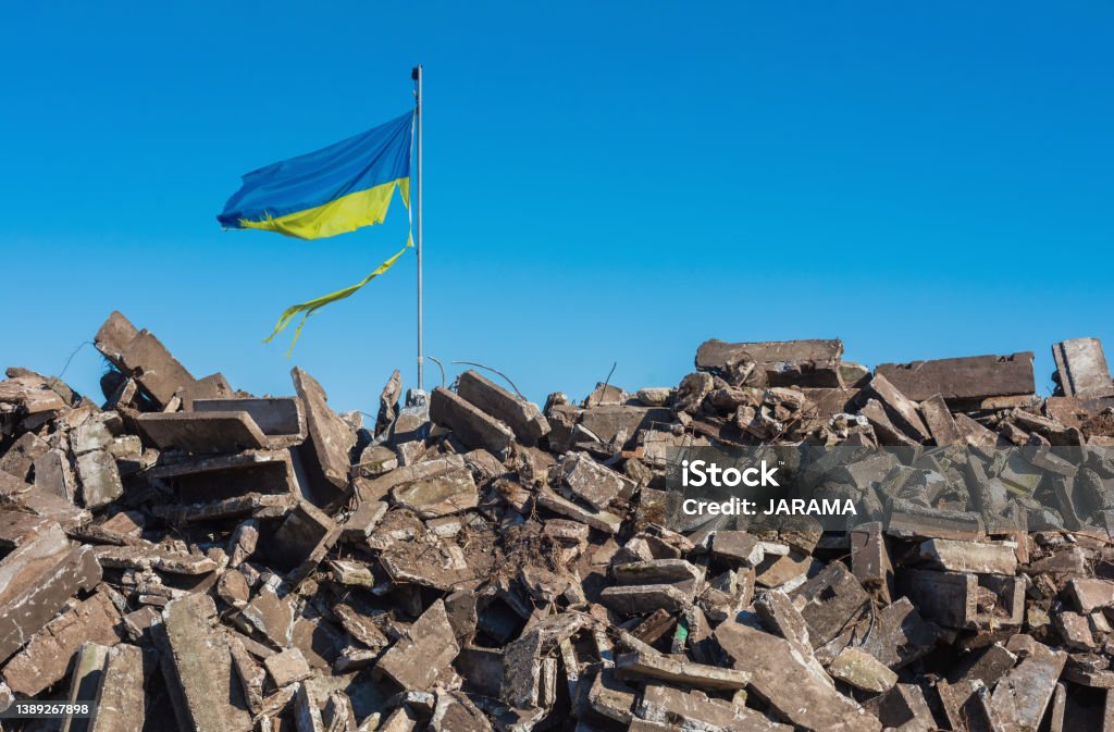 war in ukraine. Destroyed Ukrainian building and damaged flag in the wind. Concept image for the Russian attack on Ukraine. 2022 Russian Invasion of Ukraine Stock Photo