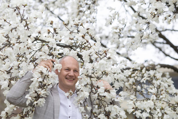schöner lächelnder mann auf dem hintergrund einer weiß blühenden magnolie - 45 hochzeitstag stock-fotos und bilder