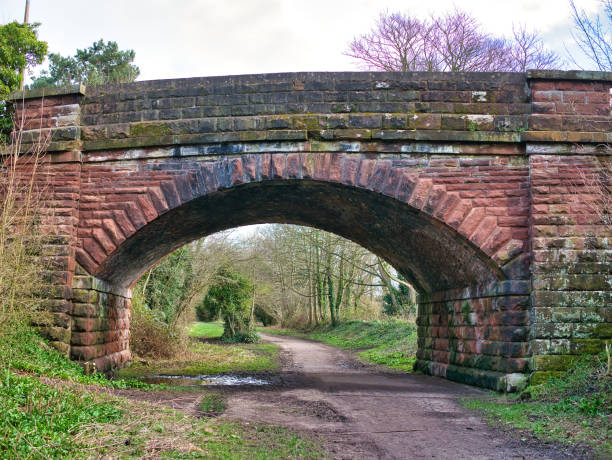 un viejo puente de piedra arenisca arqueado sobre una línea de ferrocarril en desuso, ahora wirral way, un sendero público para caminar en el noroeste de inglaterra, reino unido. - northwest england fotografías e imágenes de stock