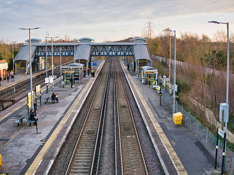 Railway tracks and platforms at Hooton Station in Wirral in north-west England. Commuters and security staff await the arrival of the next train.