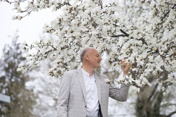 schöner lächelnder mann auf dem hintergrund einer weiß blühenden magnolie - 45 hochzeitstag stock-fotos und bilder