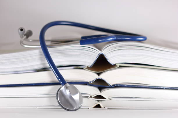 istock Blue stethoscope and stack of opened books isolated on white background. Medical professional education and information concept. 1389271478