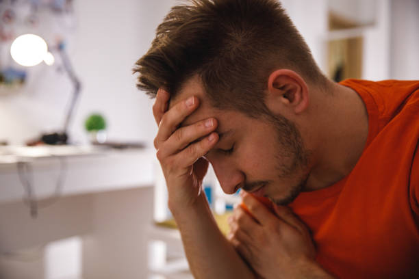 istock Distraught young man sitting with head in hand, eyes closed, worrying 1389274833