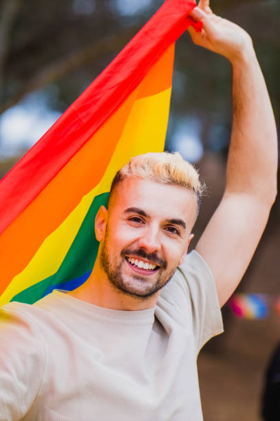 istock Gay man holding rainbow lgbt flag with a smile, vertical format 1389277384