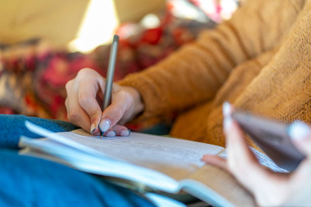 istock Close up of a woman's hand holding a mobile smartphone and using a pen while making notes in a notebook. Student studying online, reading e-book, online learning. 1389278283
