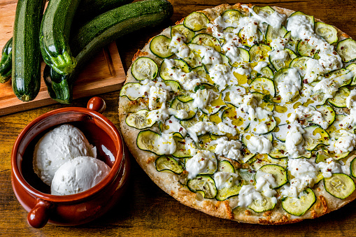 A delicious and typical Italian pizza with Zucchini and Stracchino fresh cheese, strictly cooked in a wood oven, according to the Italian tradition. Stracchino is a fresh cow's milk cheese typical of the northern regions of Italy. In 2017 the art of Neapolitan pizza was declared by UNESCO as an Intangible Cultural Heritage. Image in High Definition format.
