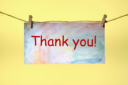 thank you text written on paper suspended from a rope on a yellow background.