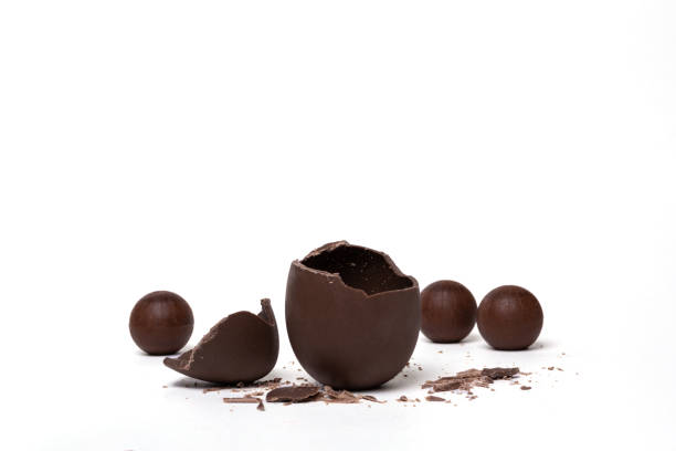 istock Cracked chocolate empty easter egg and chocolate round candies on white background. Chocolate treat for kids. 1389286182