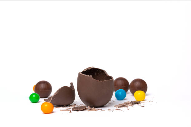 istock Cracked chocolate empty easter egg and colorful chocolate round candies on white background 1389286249
