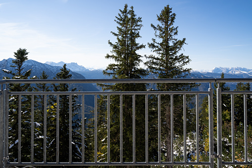 Iron railings on a viewing platform with a view of lightly snow covered fir trees and mountains on a sunny day in winter