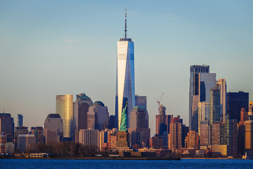 In the tranquil midst of the sea, a mesmerizing tableau unfolds. Manhattan's iconic skyline, adorned in the warm embrace of a setting sun, features the World Trade Center's twin towers, symbols of urban majesty.