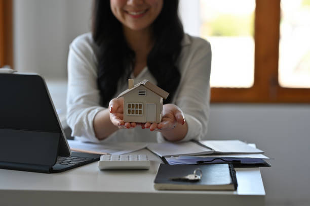 istock Close up with Real estate agent holding house model while sitting at her working place in office, Buy and loan for a house concept. 1389291803