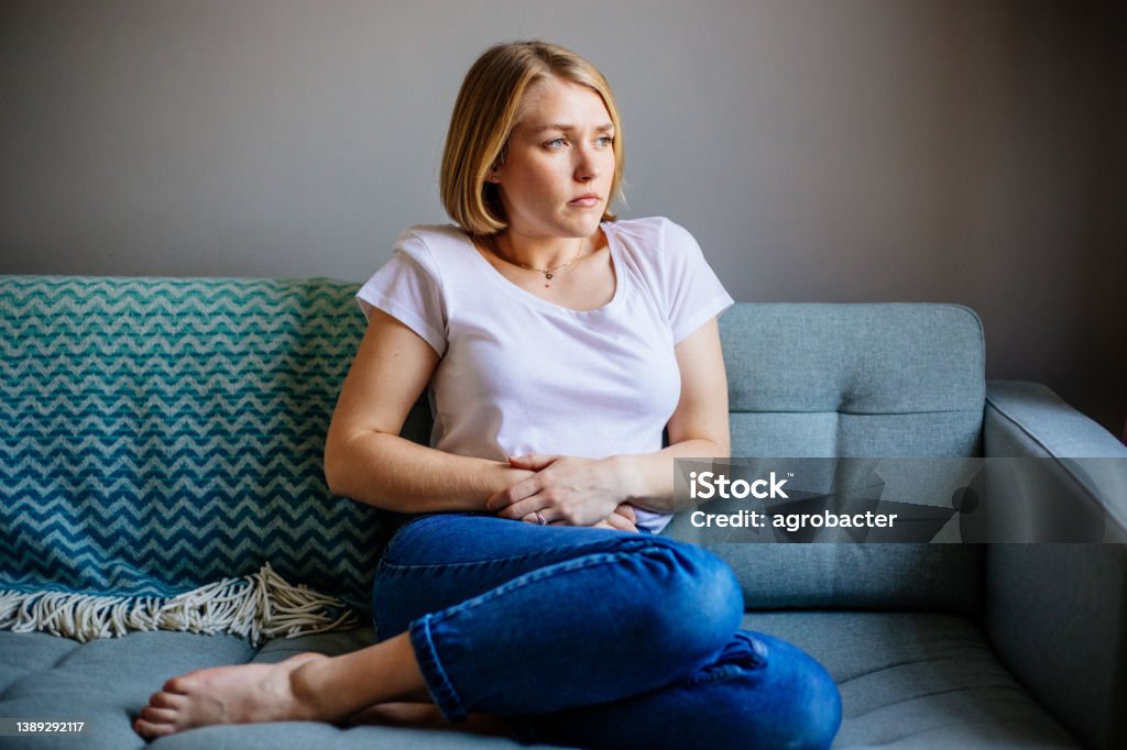 Woman experiencing stomach pain while lying on the sofa at home Stomachache Stock Photo