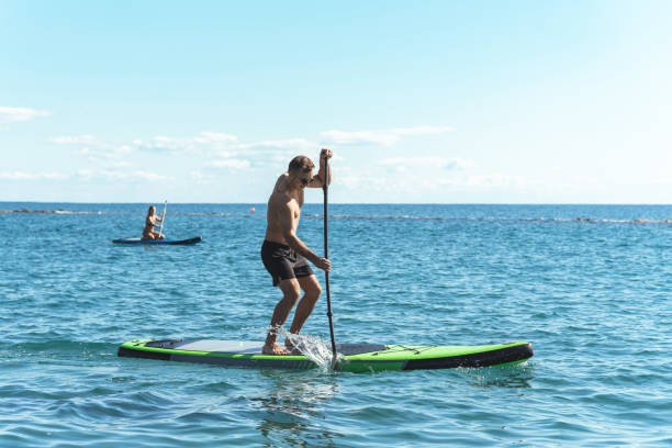 istock Young male surfer riding standup paddleboard in ocean. 1389292795