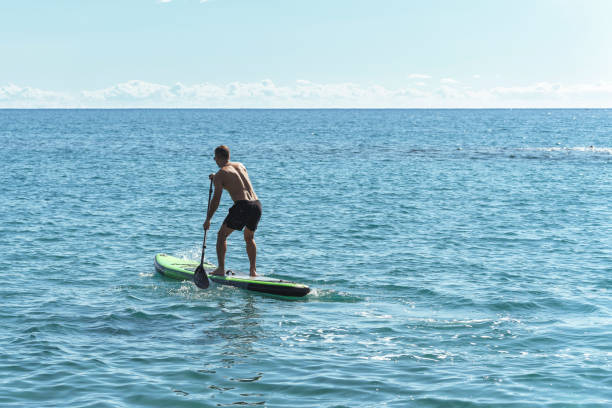 istock Young male surfer riding standup paddleboard in ocean. 1389292823