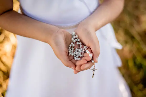Hands of prying girl going to the first holy communion, close up on rosary on child's hands.